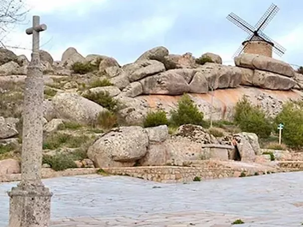 Ermita y cruz de piedra junto a un molino entre rocas