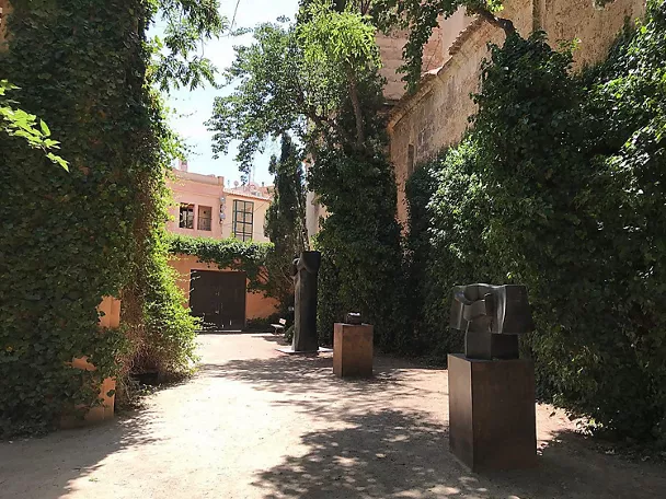 Sendero ajardinado con esculturas abstractas de metal entre muros cubiertos de hiedra.