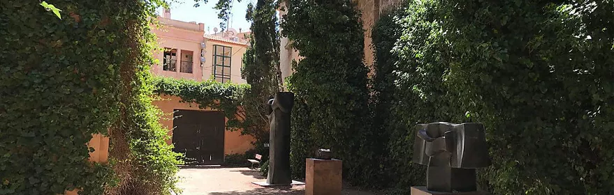 Sendero ajardinado con esculturas abstractas de metal entre muros cubiertos de hiedra.