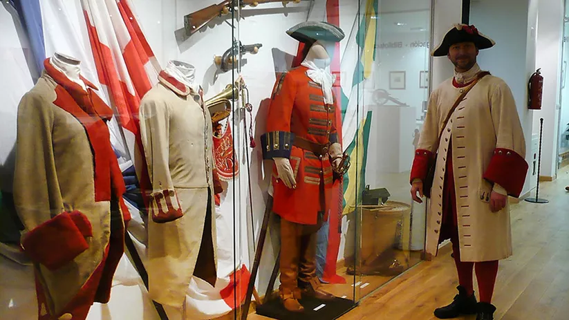Vitrina con uniformes militares históricos y armas antiguas en exposición.