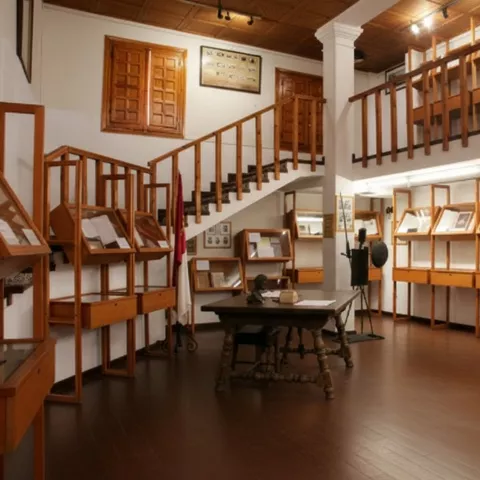 Sala de museo con vitrinas de madera, mesa central y balcón interior.