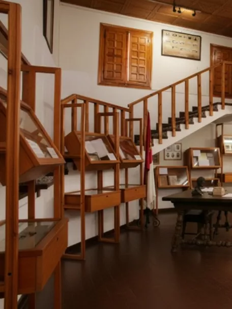 Sala de museo con vitrinas de madera, mesa central y balcón interior.