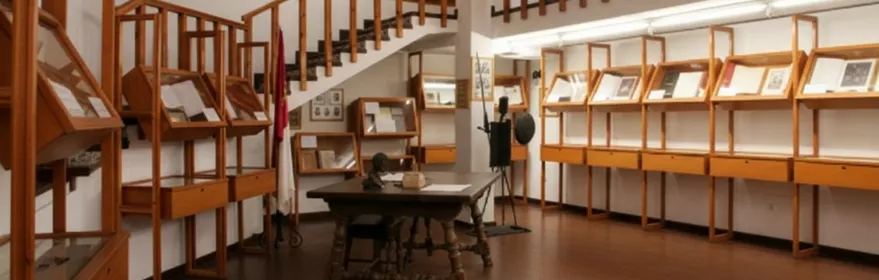 Sala de museo con vitrinas de madera, mesa central y balcón interior.