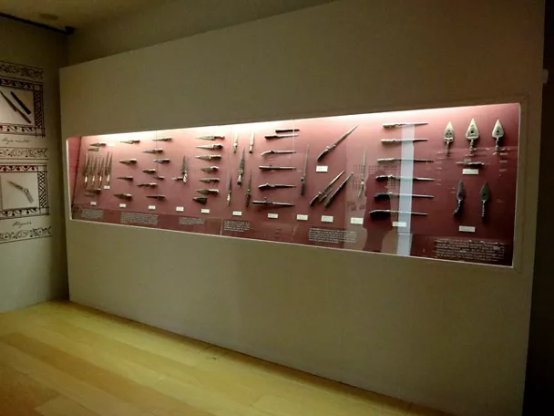 Panel expositivo con navajas y herramientas históricas iluminadas en una sala de museo.