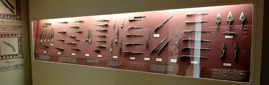 Panel expositivo con navajas y herramientas históricas iluminadas en una sala de museo.