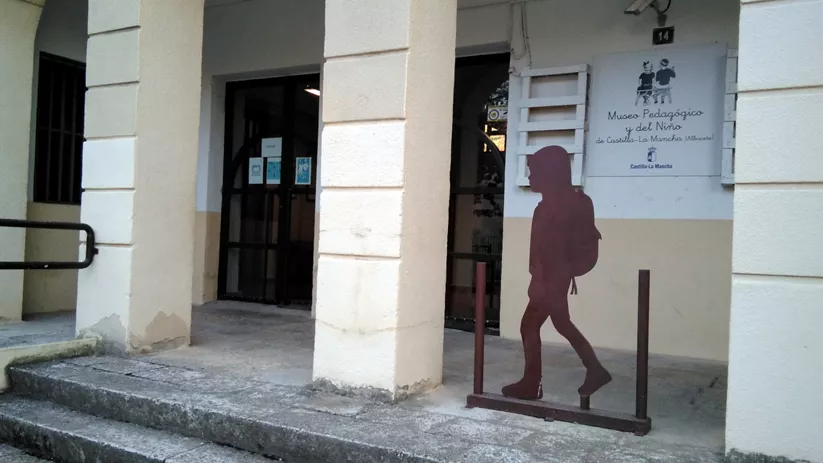 Entrada a edificio con soportales y silueta metálica de un niño con mochila.