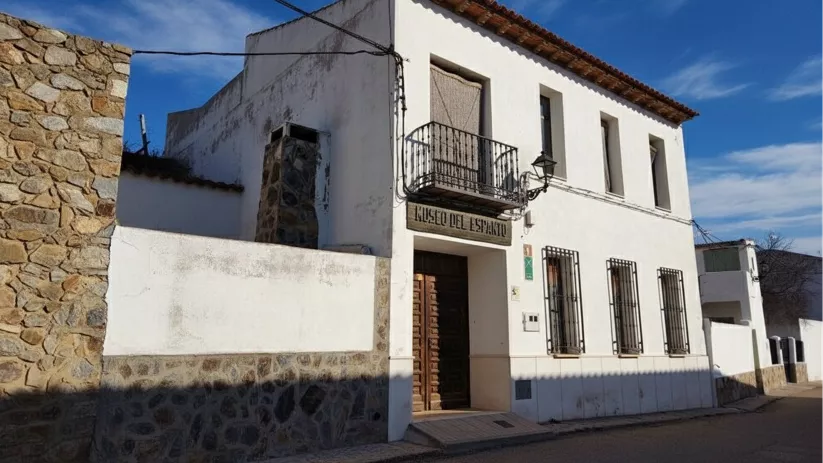 Fachada blanca de edificio tradicional con balcón y puerta de madera en calle estrecha.
