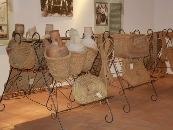 Exposición de recipientes de barro y cestas de fibra vegetal sobre soportes metálicos.