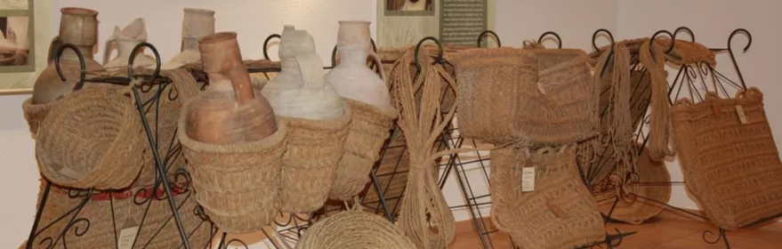 Exposición de recipientes de barro y cestas de fibra vegetal sobre soportes metálicos.