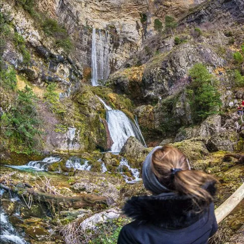 Imagen de una mujer observando la montaña por el que cae una cascada del nacimiento del río