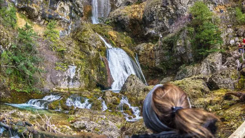 Imagen de una mujer observando la montaña por el que cae una cascada del nacimiento del río