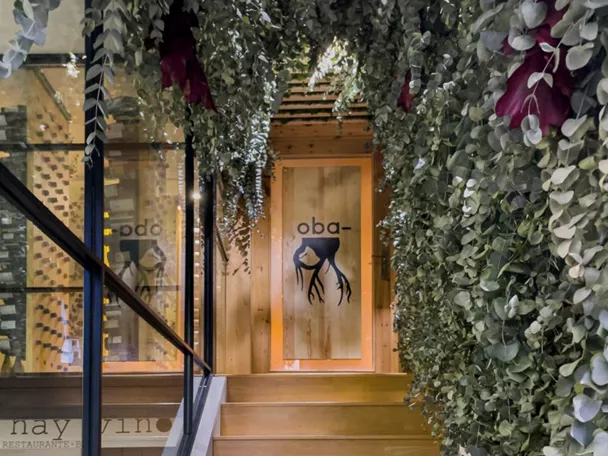 Entrada a espacio gastronómico con escaleras de madera y vegetación colgante.
