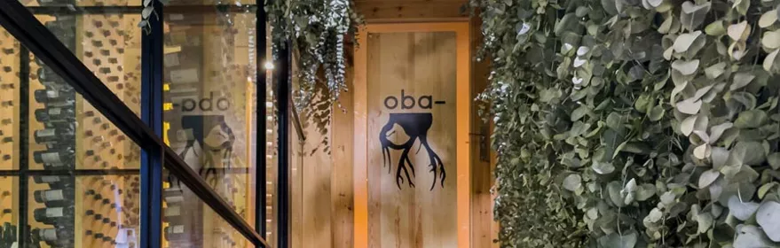 Entrada a espacio gastronómico con escaleras de madera y vegetación colgante.