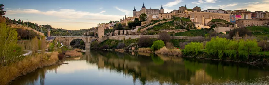 Vista panorámica de ciudad histórica con río, puente de piedra y edificios en la colina