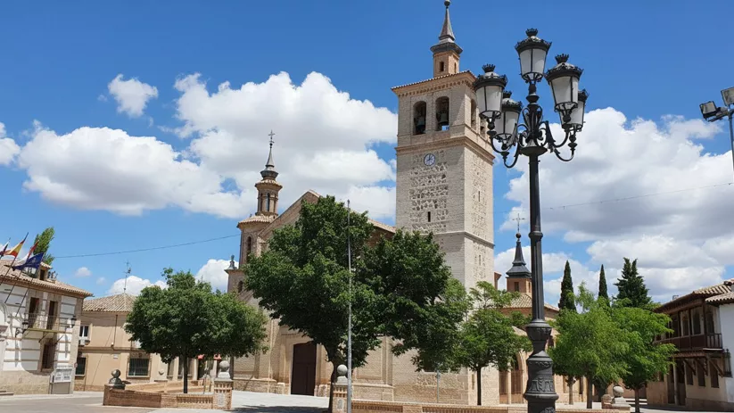 Plaza arbolada con iglesia de gran torre y farola ornamental