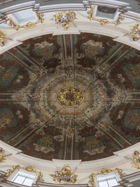 Cúpula interior decorada con frescos circulares, molduras blancas y detalles dorados.