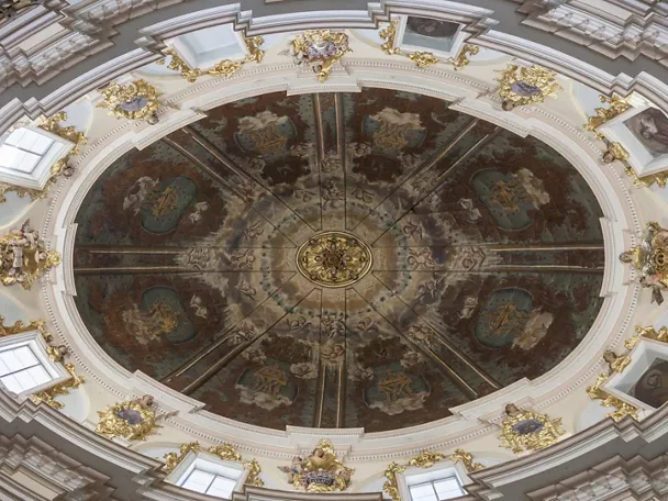 Cúpula interior decorada con frescos circulares, molduras blancas y detalles dorados.