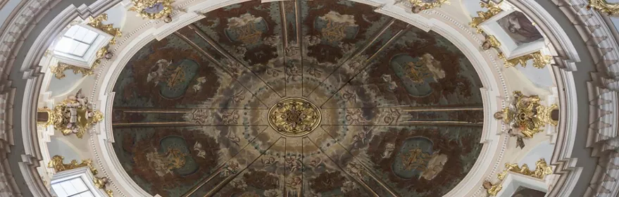 Cúpula interior decorada con frescos circulares, molduras blancas y detalles dorados.