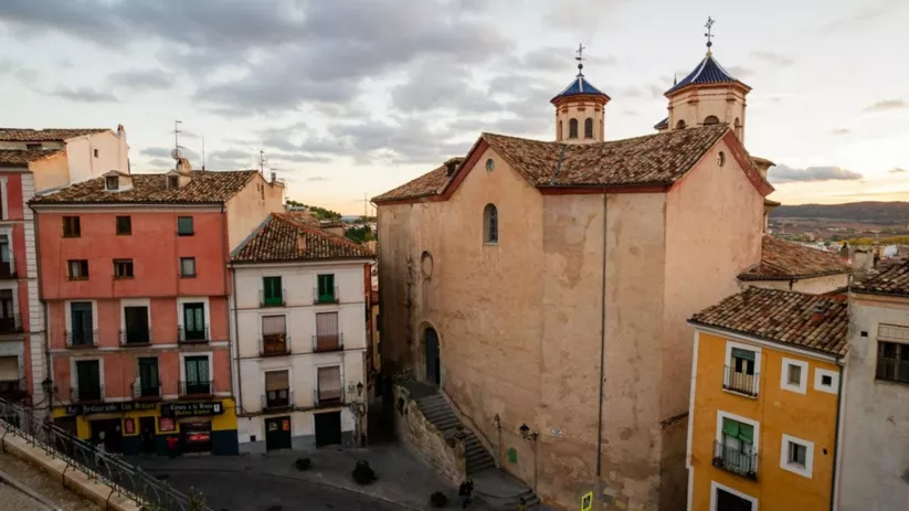 Vista aérea de edificio histórico con tejados de teja y dos torres, rodeado de casas tradicionales.