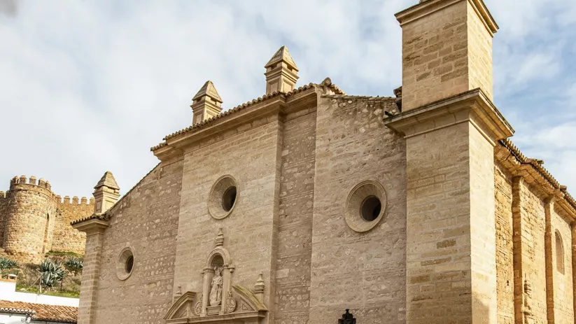 Fachada lateral de iglesia de piedra con muralla al fondo