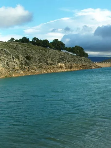Embalse rodeado de colinas rocosas bajo un cielo parcialmente nublado.