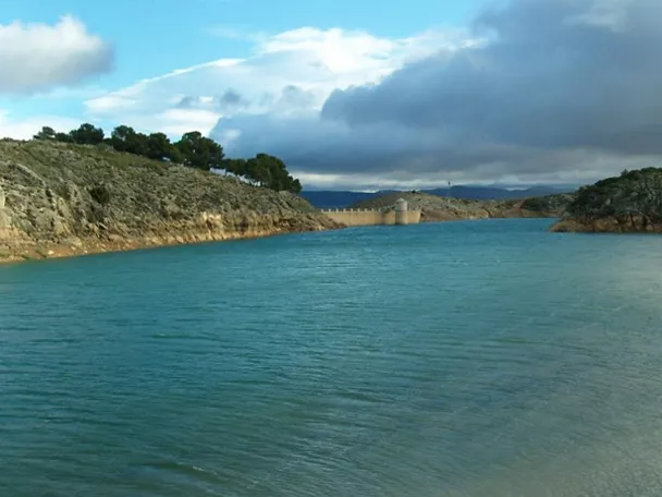 Embalse rodeado de colinas rocosas bajo un cielo parcialmente nublado.