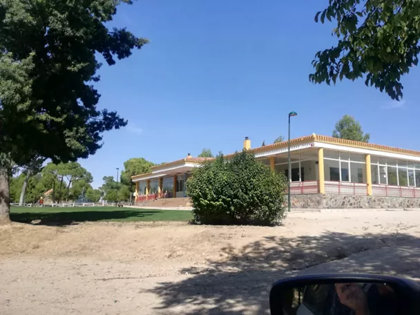Edificio de una planta rodeado de zonas verdes y arbolado.