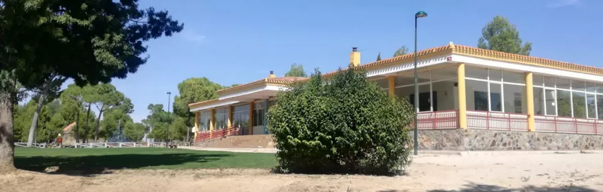 Edificio de una planta rodeado de zonas verdes y arbolado.