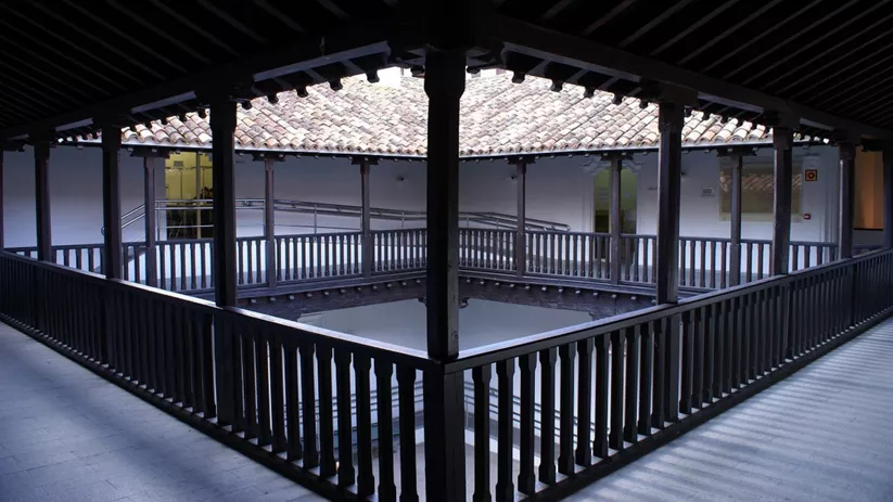 Galería interior con barandillas de madera alrededor de un patio central.