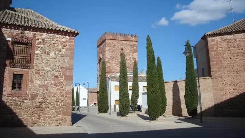 Torre de piedra al fondo de una plaza con cipreses