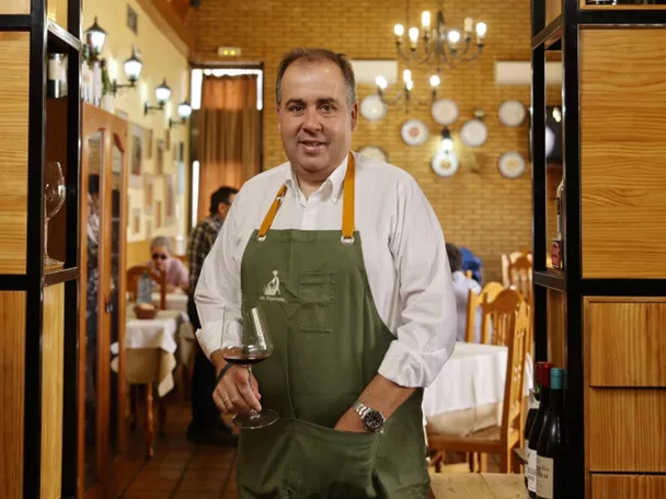 Hombre con delantal sostiene una copa de vino en el interior de un restaurante.