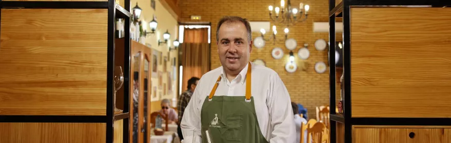 Hombre con delantal sostiene una copa de vino en el interior de un restaurante.