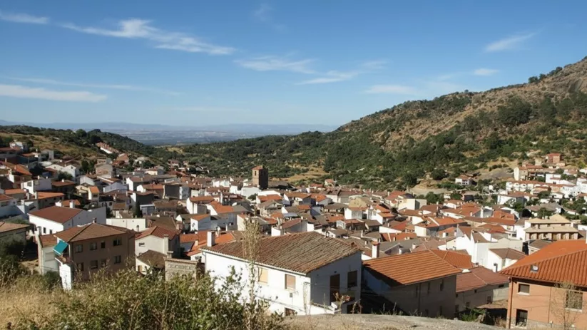 Una vista aérea de un pueblo de montaña con muchas casas de tejados rojos agrupadas en un valle entre colinas boscosas.