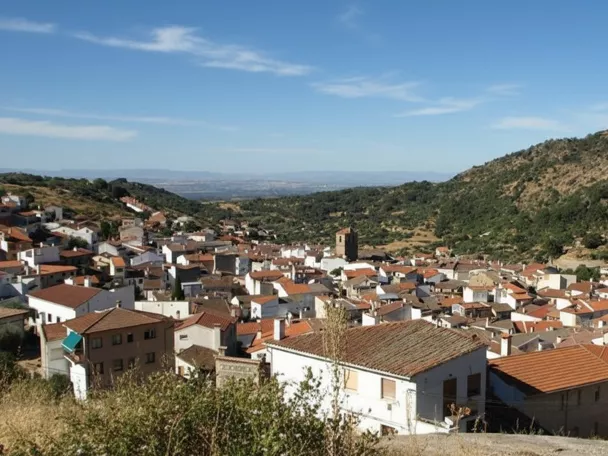 Una vista aérea de un pueblo de montaña con muchas casas de tejados rojos agrupadas en un valle entre colinas boscosas.
