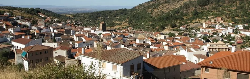 Una vista aérea de un pueblo de montaña con muchas casas de tejados rojos agrupadas en un valle entre colinas boscosas.