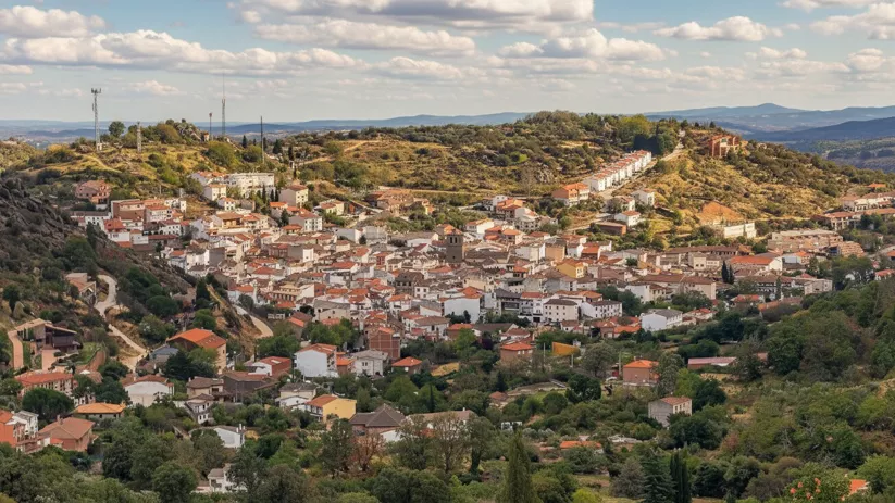 Una vista panorámica de un pueblo de casas blancas y tejados rojos enclavado en una ladera de colinas cubiertas de vegetación.