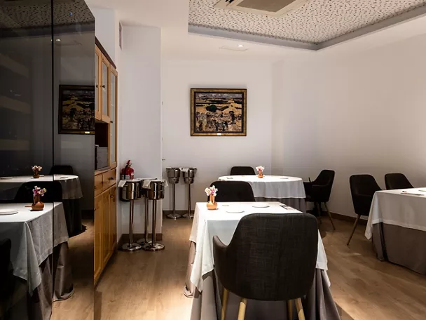 Comedor elegante con mesas vestidas, sillas tapizadas y luz cálida.