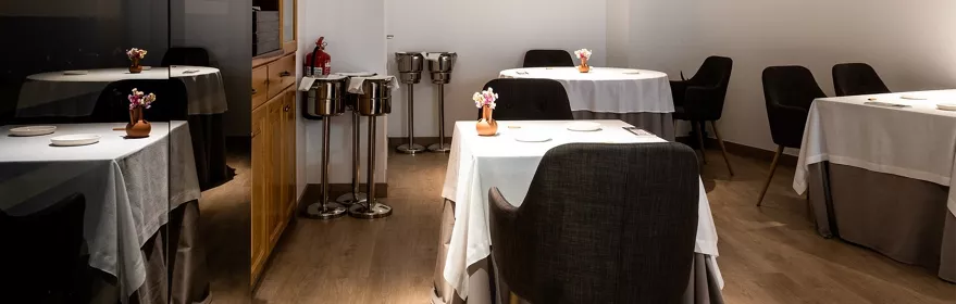 Comedor elegante con mesas vestidas, sillas tapizadas y luz cálida.