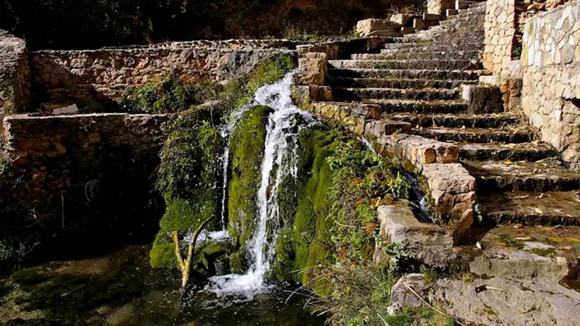 Cascada natural entre muros de piedra y escalones.