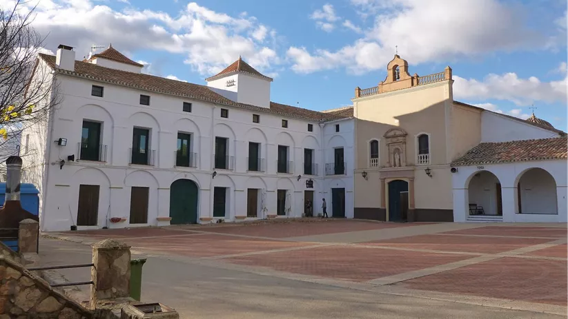 Plaza empedrada con edificio religioso y pórticos blancos bajo cielo despejado.