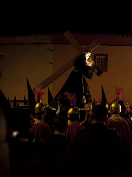 Procesión nocturna con pasos religiosos iluminados y penitentes con capirotes.