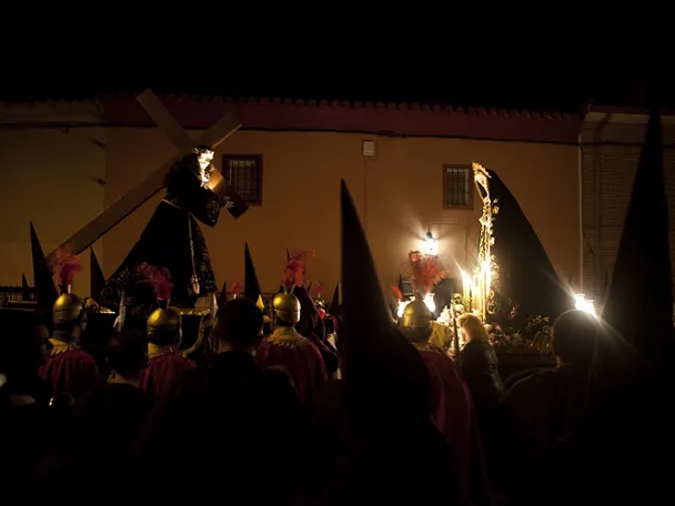 Procesión nocturna con pasos religiosos iluminados y penitentes con capirotes.
