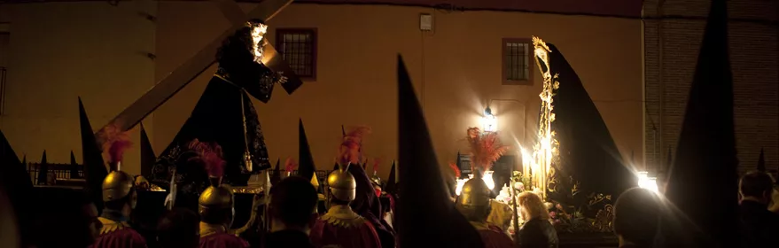 Procesión nocturna con pasos religiosos iluminados y penitentes con capirotes.