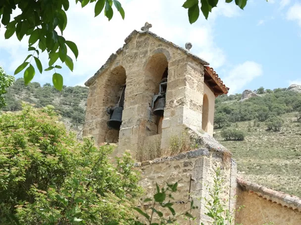 Espadaña de piedra con campanas entre vegetación y colinas