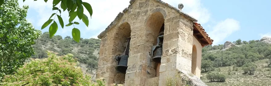 Espadaña de piedra con campanas entre vegetación y colinas