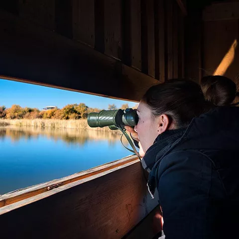 Imagen de una persona con unos prismáticos mirando una laguna