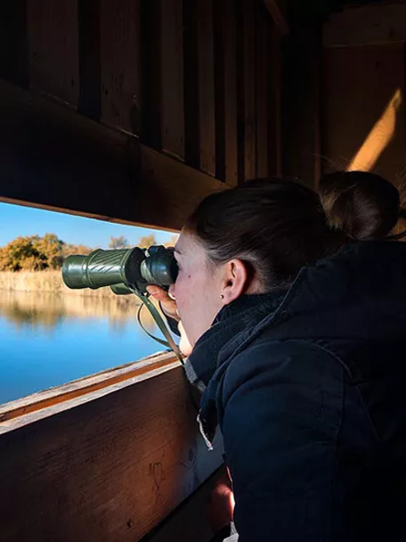Imagen de una persona con unos prismáticos mirando una laguna