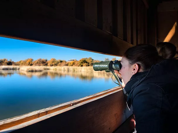 Imagen de una persona con unos prismáticos mirando una laguna