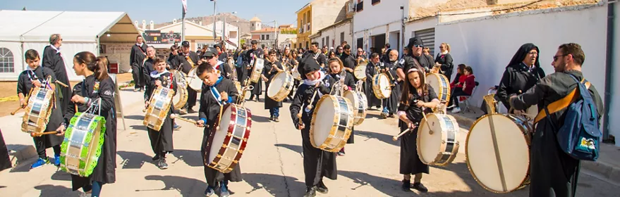 Niños y adultos tocando tambores en una celebración popular al aire libre.