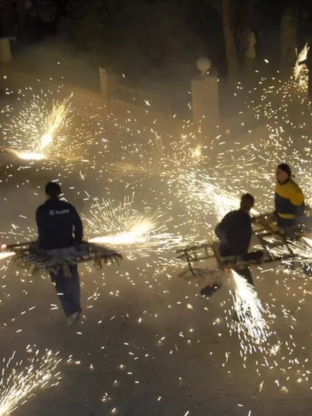 Personas portando estructuras con fuegos artificiales que lanzan chispas.